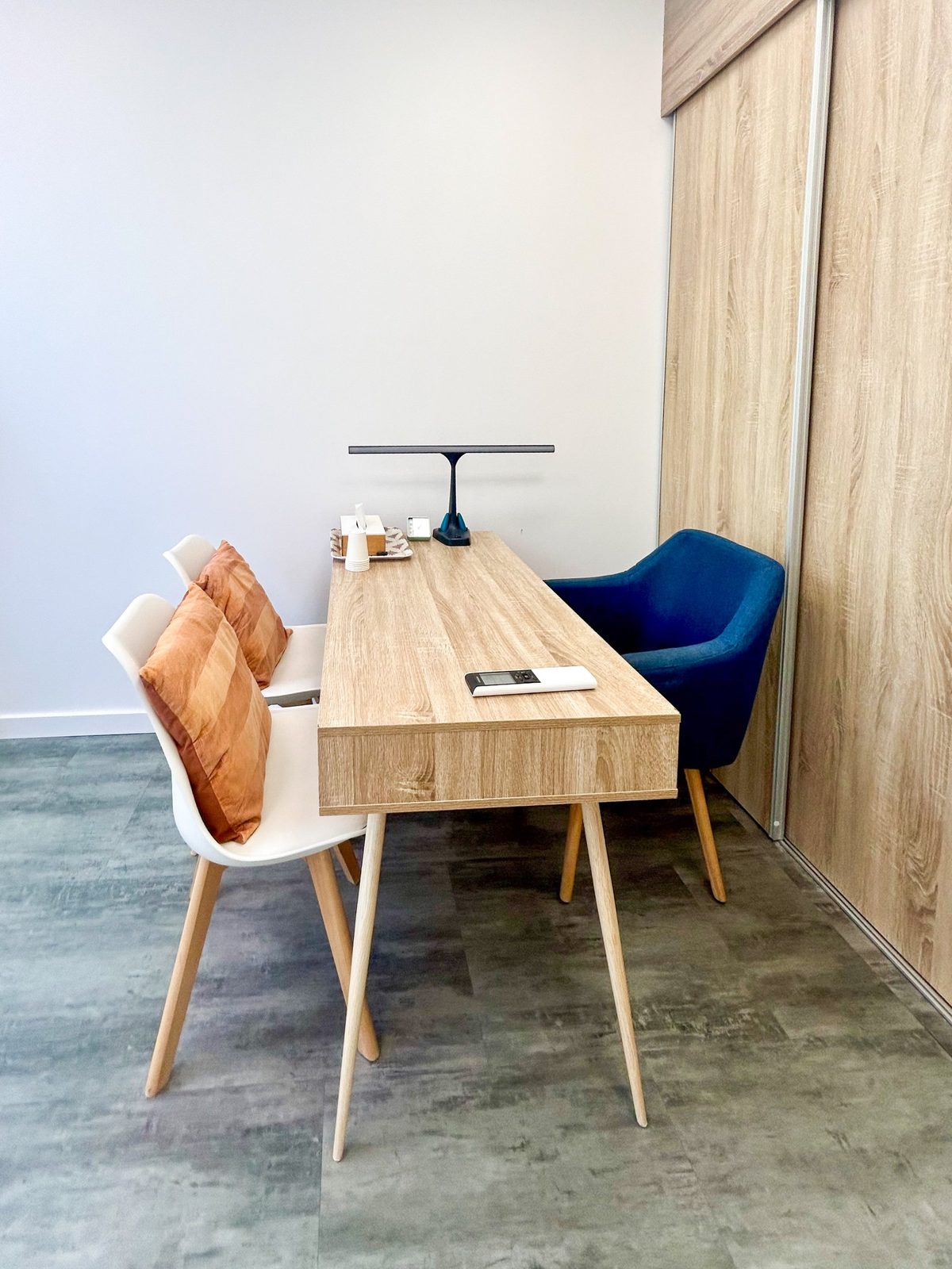 Le bureau du cabinet : deux chaises blanches avec coussins terracotta, une table en bois et un fauteuil bleu
